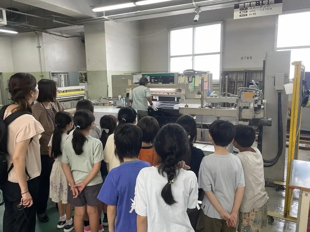 実際に印刷機械が動いている様子を学生たちが少し離れた場所から見学している写真