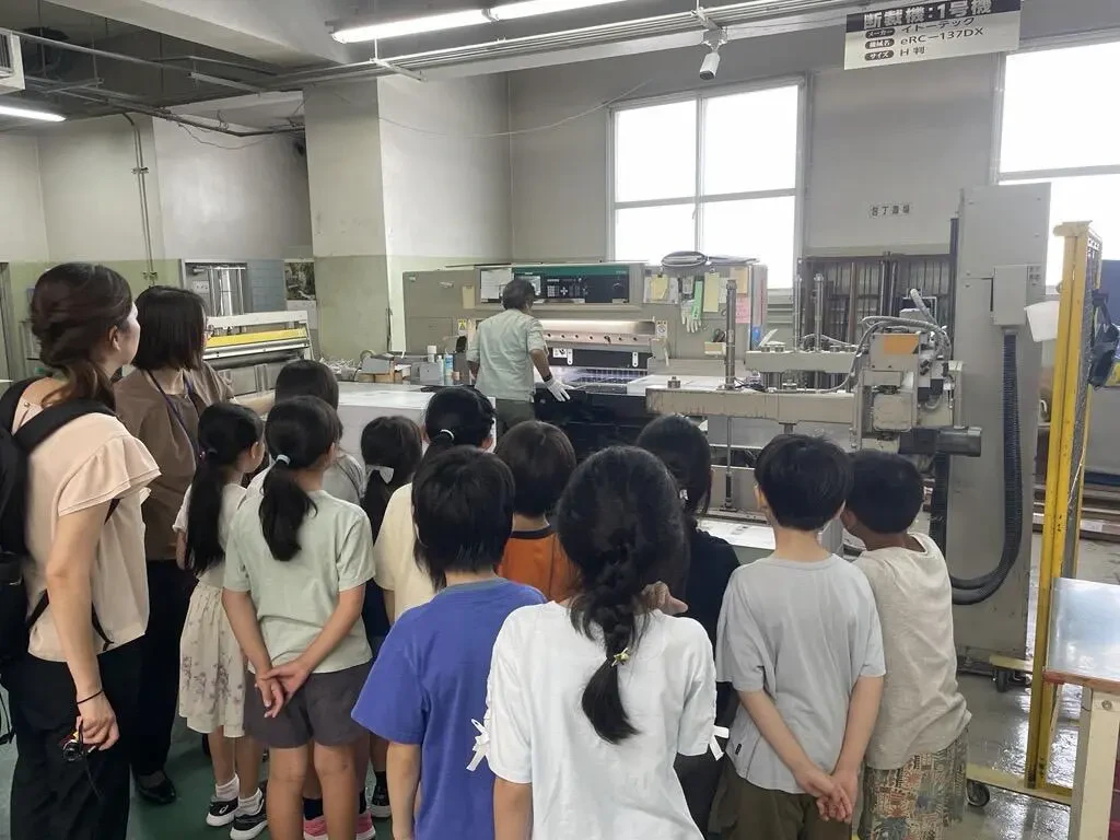 実際に印刷機械が動いている様子を学生たちが少し離れた場所から見学している写真