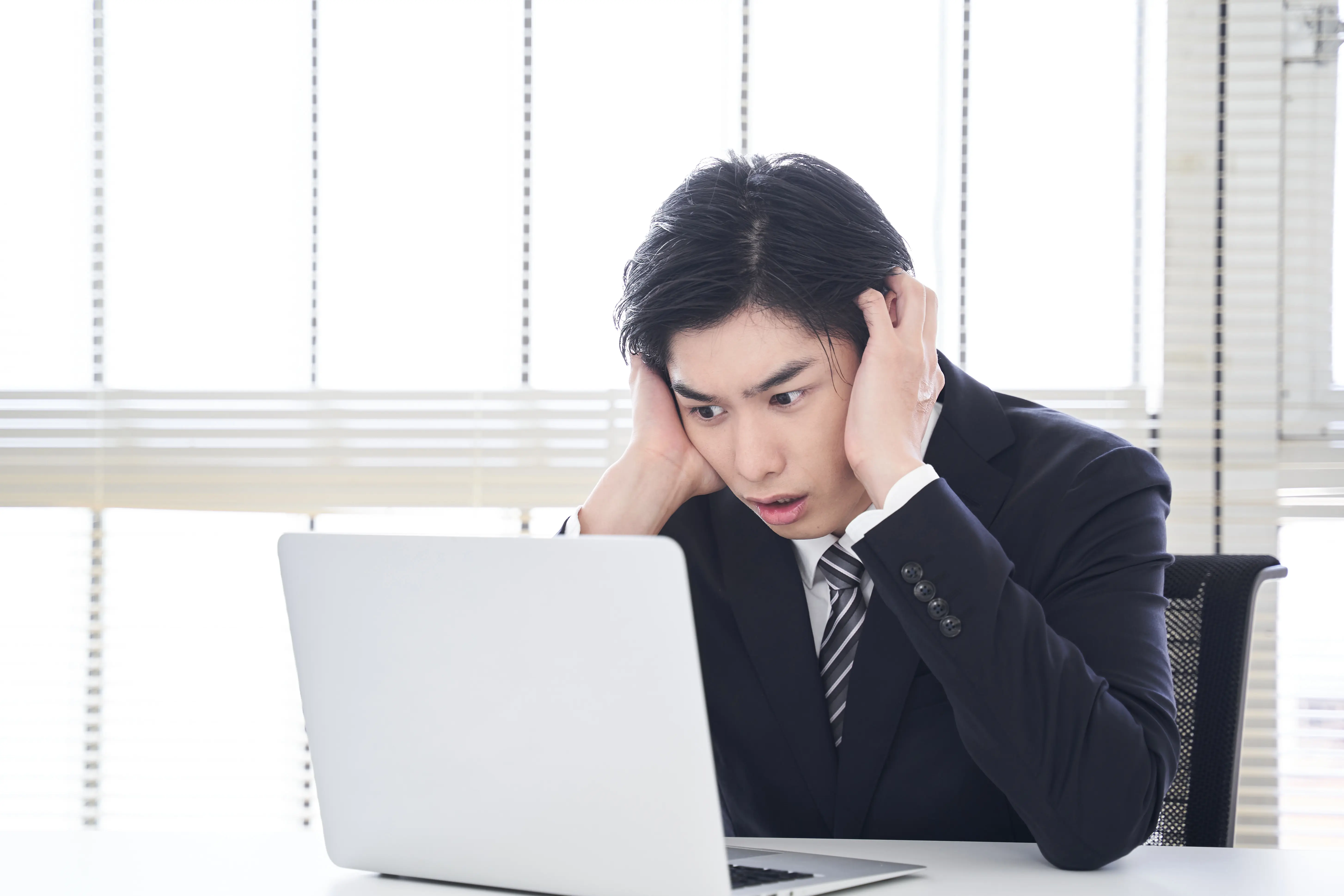 ノートパソコンの前で頭を抱えている男性のイメージ
