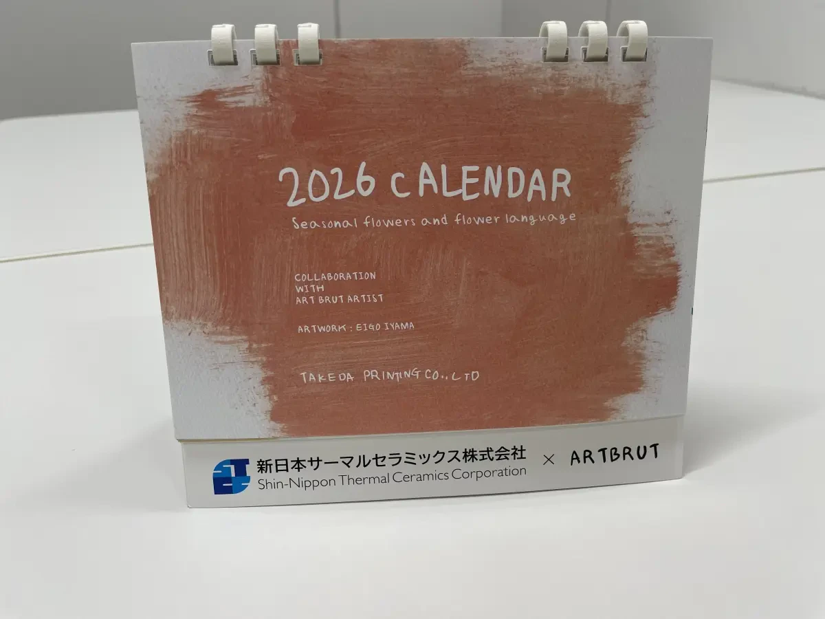 完成したアール・ブリュット卓上カレンダーの写真。表紙はくすみのあるオレンジ色の背景に白文字で「2026 CALENDAR」と書かれたシンプルかつPOPさも感じるデザイン