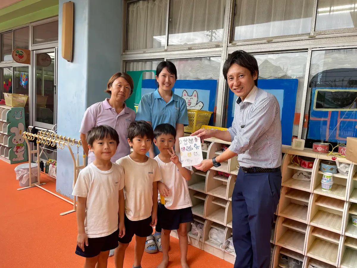 高辻幼稚園にて、園児たちと先生方に「残紙ノート」を渡している様子の写真