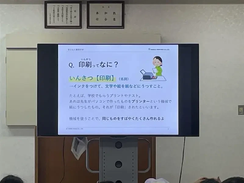 会議室のモニターに「印刷ってなに?」の見出しに印刷について説明された文章が掲載されたスライドが映っている写真