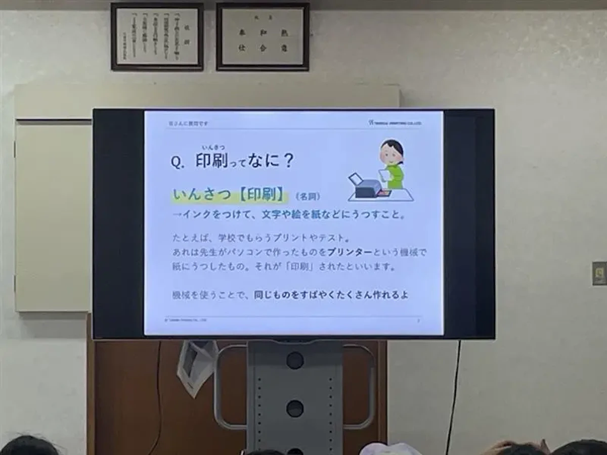 会議室のモニターに「印刷ってなに？」の見出しに印刷について説明された文章が掲載されたスライドが映っている写真